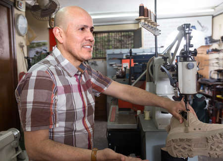 Mature male sewing leather boots on stitch lathe in workshopの写真素材