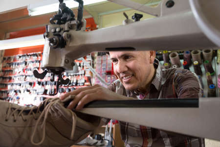 senior specialist stitching shoes on leather sewing machine at factory. fokus on manの写真素材