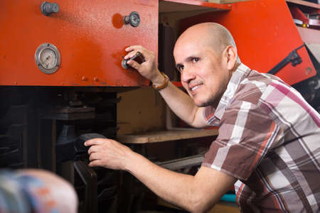 Professional smiling craftsman stitching footwear on machine in shoe atelierの写真素材