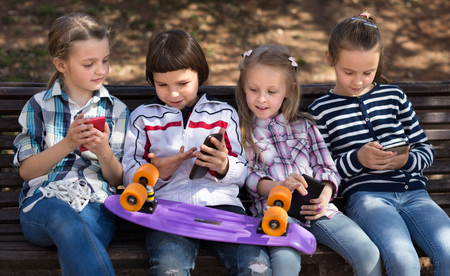 ordinary children playing with the phone on bench outdoors. focus on the left childrenの写真素材