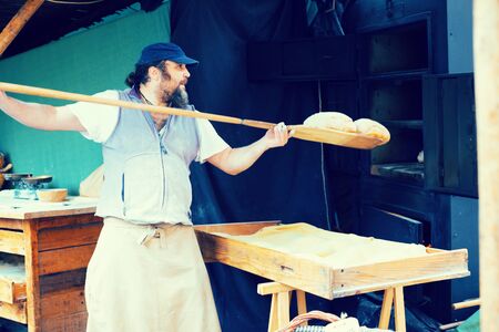 male baker puts bread on the shovel into the ovenの写真素材