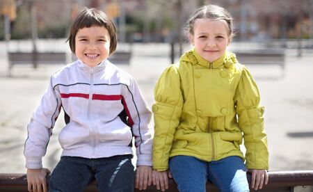 Boy with blonde girl sitting on park bench outdoors in springの写真素材