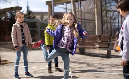 children's games. blonde Girl jumps over the rope in park in springの写真素材