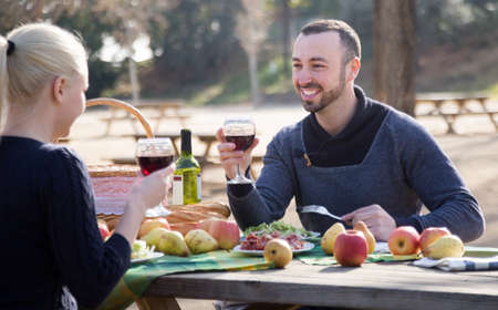 smiling young couple drinking wine and talking on picnic at parkの写真素材