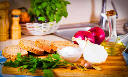 Wheat bread, salt, onions and parsley lying on a wooden cutting boardの写真素材
