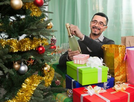 Old happy mature man near Christmas holding  champagne bottleの写真素材