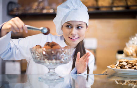 Happy shopgirl offering different pastry for saleの写真素材