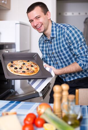 Young smilingman preparing delicious pizza in oven at homeの写真素材
