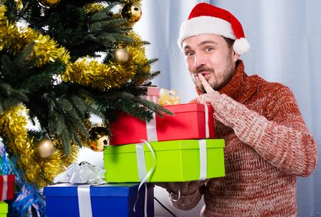 Portrait of man wearing Santa secretly puts gifts under the Christmas treeの写真素材