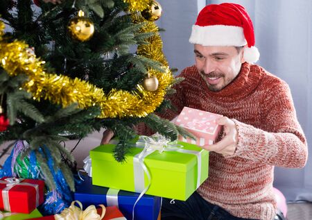Portrait of funny guy wearing Santa puts gifts under the Christmas treeの写真素材