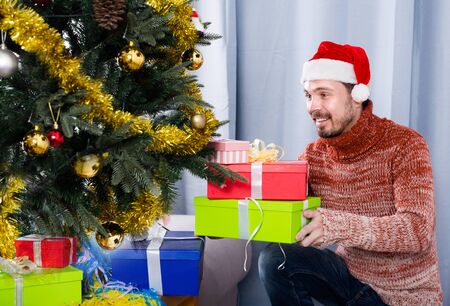 man wearing Santa puts New Year gifts under the Christmas treeの写真素材