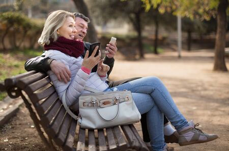 Senor man and woman exchanging phone numbers during outdoor dateの写真素材