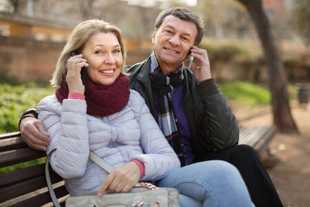 Happy elderly couple with mobile phones in sunny autumn dayの写真素材
