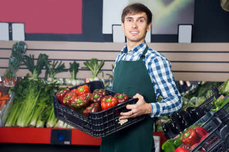 Male grocery worker selling fresh vegetables and herbs at local marketの写真素材