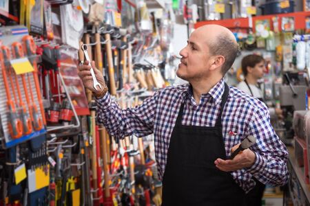 Mature seller offering working tooling in household storeの写真素材