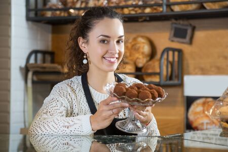Portrait of young attractive female pastry chef holding chocolate candy in a crystal vaseの写真素材