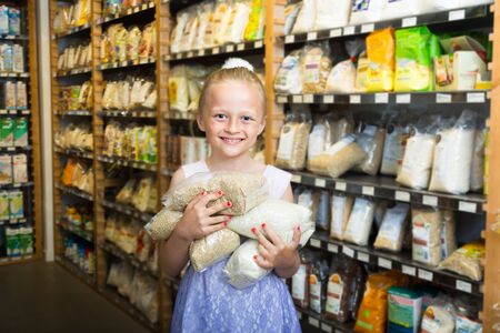 blonde girl posing with packs of rice in supermarketの写真素材