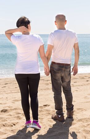 Mature couple embracing looking at the sea on the beach in summer on leaveの写真素材