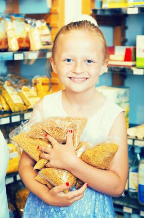 blonde girl holds lot of spaghetti packages in storeの写真素材