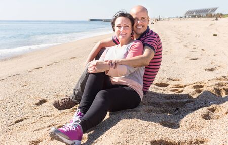 smiling man and a middle-aged woman sitting on the beachの写真素材