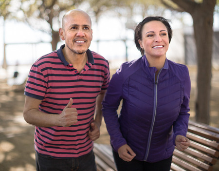 man and middle-aged woman running in park. focus on manの写真素材
