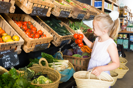blonde girl choosing  tomatoes in vegetable shop. on labels of product names in Catalanの写真素材
