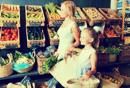 blonde mother and daughter choose vegetables in vegetable shop. on labels of product names in Catalanの写真素材