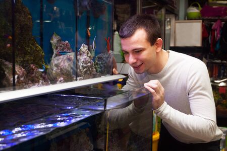 Portrait of young guy selecting tropical fish in petshopの写真素材
