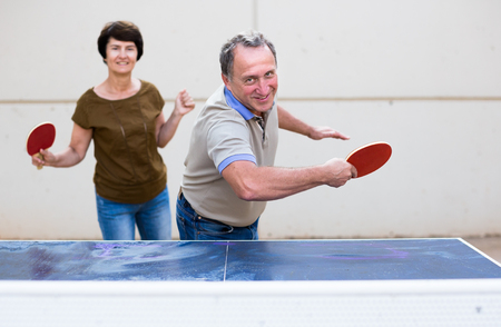 Happy mature man and woman playing table tennisの写真素材