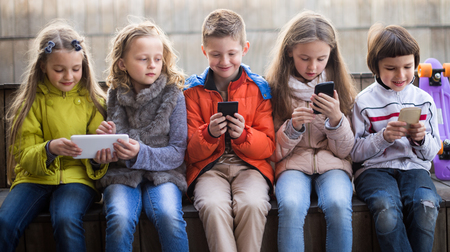 girls and boy with smartphones on bench in park in autumnの写真素材