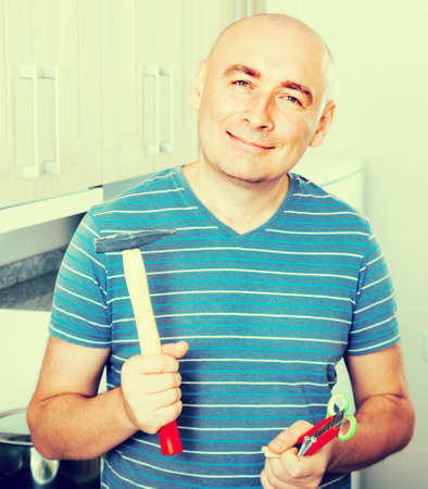 ordinary guy in striped shirt posing with hammer in his handsの写真素材