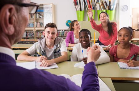 schoolgirl raising her hand to answer a lesson. Focus on girl on right aboveの写真素材