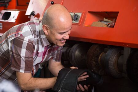 Professional workman polishing footwear on machine in shoe atelierの写真素材