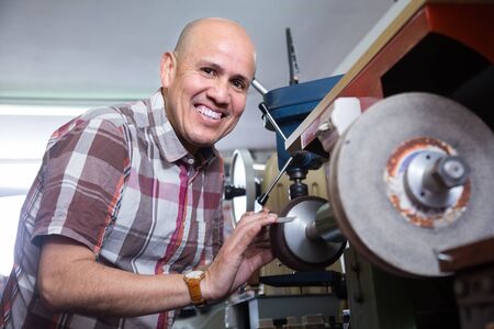 Portrait of Mature workman resharpering knives on interlock spiral wheel system machineの写真素材