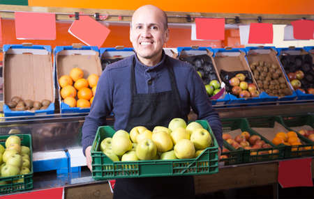 active mature male vendor selling apples in the grocery storeの写真素材