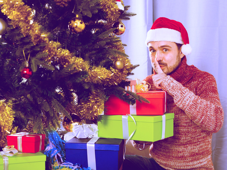 guy wearing Santa secretly puts gifts under the Christmas treeの写真素材