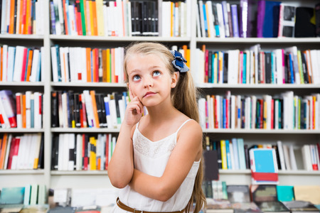 pensive girl surprised chooses a book in the libraryの写真素材