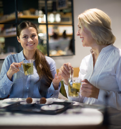 Portrait of two women with tea and chocolates in cafeの写真素材