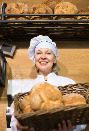 Mature woman selling fresh pastry and baguettes in shopの写真素材