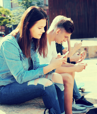 group of teenagers play in smartphones in schoolyardの写真素材
