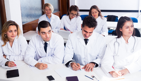 Students in white coats listen to lecture in audienceの写真素材
