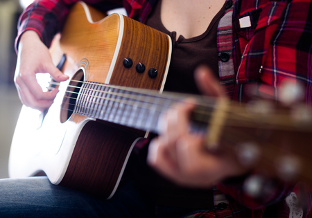 Close-up girl tuning guitar. Focus on strings of guitarの写真素材