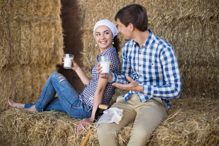 young couple of farmers drinking milk in hayloft on farm