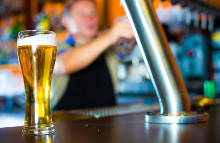 glass of beer on bar counter against background of friendly elderly bartenderの写真素材