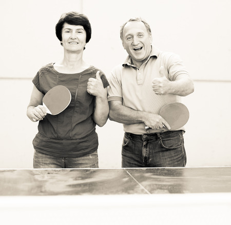 Portrait of elderly couple showing thumb up with rackets for table tennisの写真素材