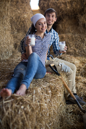 young couple of farmers drinking milk in hayloft on farmの写真素材