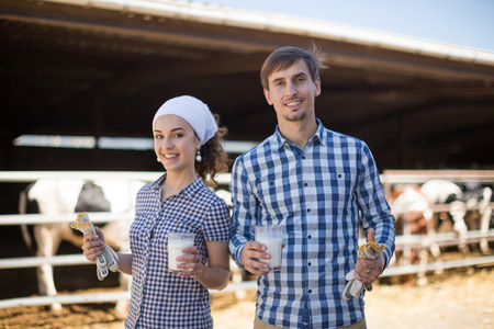 young country couple of farmers posing with glass of milk at cowfarmの写真素材