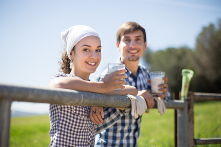 young country couple of farmers drink milk in field near fencの写真素材