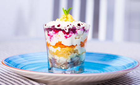 verrin glass with delicious Russian salad herring under fur coat from vegetables on blue plateの写真素材