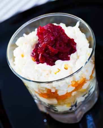 Russian salad herring under fur coat from vegetables in verrin on black plateの写真素材